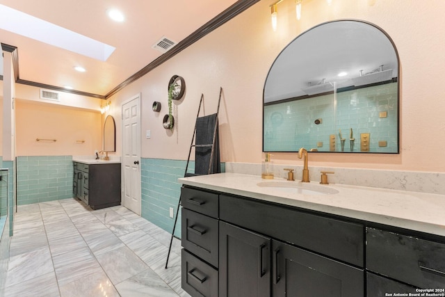 bathroom with a skylight, ornamental molding, vanity, a shower, and tile walls