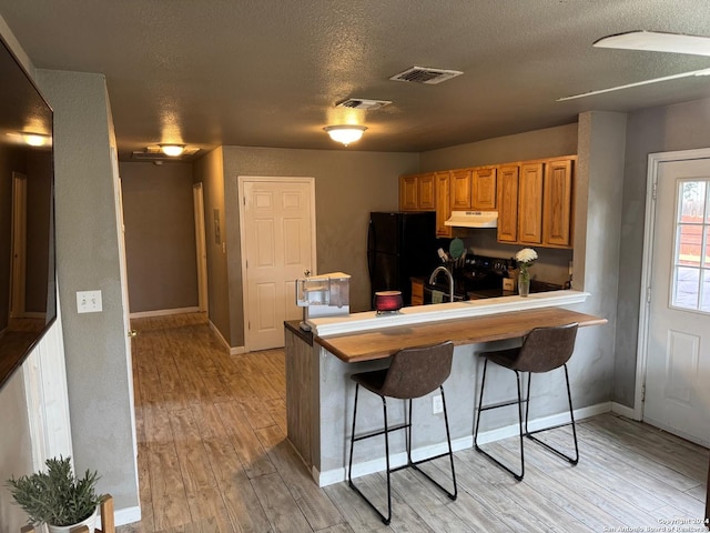 kitchen featuring kitchen peninsula, a kitchen breakfast bar, a textured ceiling, black appliances, and light hardwood / wood-style floors