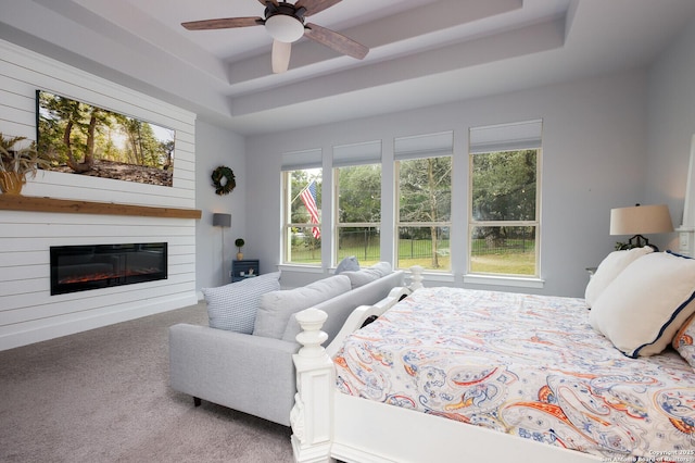 carpeted bedroom with ceiling fan, a raised ceiling, and a fireplace