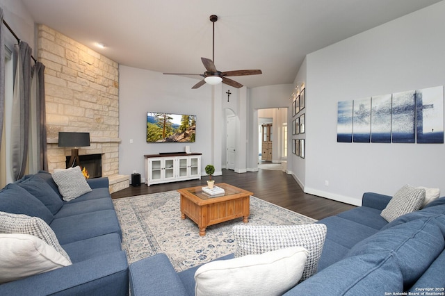 living room with ceiling fan, dark wood-type flooring, and a stone fireplace