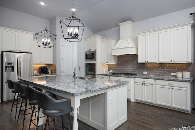 kitchen featuring custom exhaust hood, appliances with stainless steel finishes, a kitchen island with sink, lofted ceiling, and sink