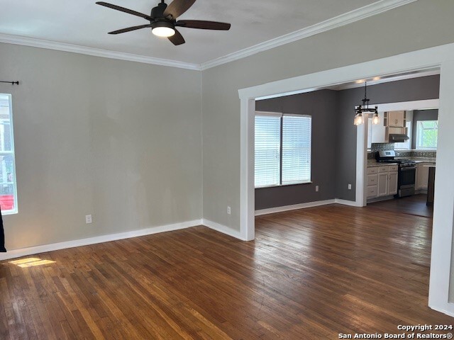 unfurnished living room featuring dark hardwood / wood-style flooring, ceiling fan with notable chandelier, and crown molding