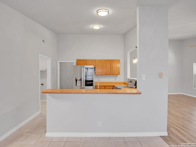 kitchen featuring light brown cabinets, kitchen peninsula, stainless steel appliances, and light tile patterned floors