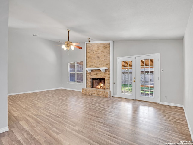 unfurnished living room with french doors, a brick fireplace, ceiling fan, light hardwood / wood-style floors, and lofted ceiling