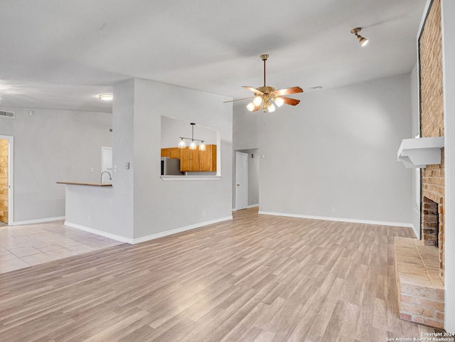 unfurnished living room featuring ceiling fan, sink, a fireplace, light hardwood / wood-style floors, and lofted ceiling