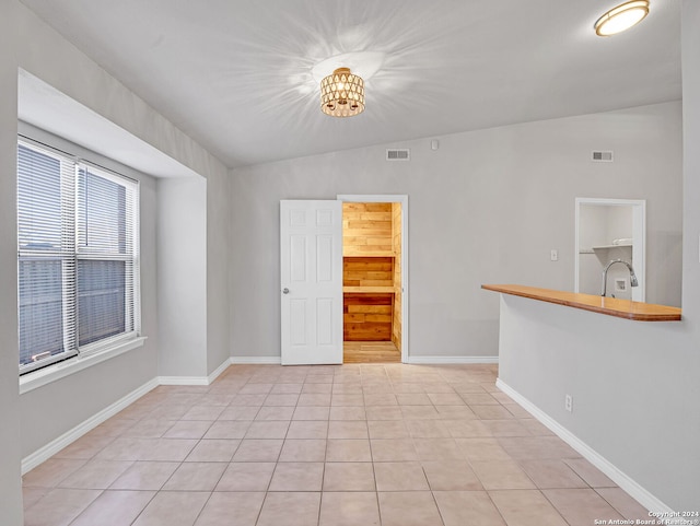 tiled empty room with sink, a chandelier, and lofted ceiling