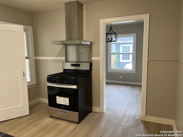 kitchen featuring stainless steel gas range oven, wall chimney range hood, pendant lighting, an inviting chandelier, and light hardwood / wood-style floors