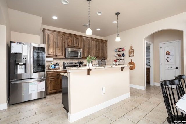 kitchen featuring light stone countertops, appliances with stainless steel finishes, backsplash, a kitchen island with sink, and light tile patterned flooring