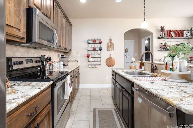 kitchen with appliances with stainless steel finishes, tasteful backsplash, light stone counters, sink, and light tile patterned floors