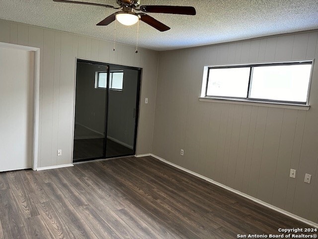 spare room with wooden walls, ceiling fan, dark wood-type flooring, and a textured ceiling