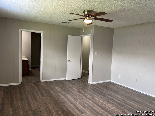 unfurnished bedroom with a textured ceiling, ceiling fan, ensuite bathroom, and dark hardwood / wood-style floors