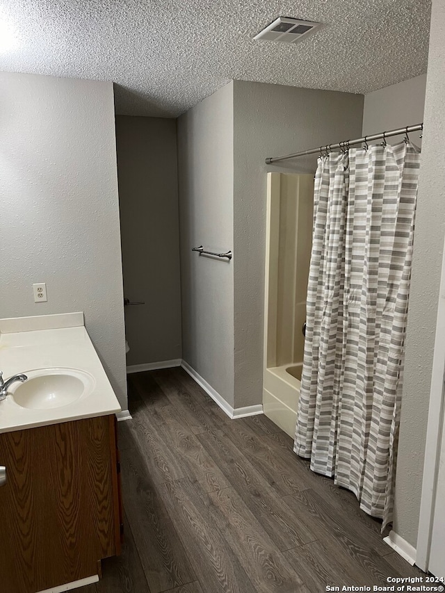 bathroom with hardwood / wood-style floors, vanity, shower / bathtub combination with curtain, and a textured ceiling