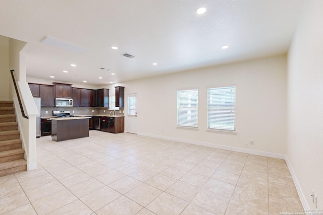 kitchen with white refrigerator, light tile patterned floors, tasteful backsplash, dark brown cabinets, and a kitchen island