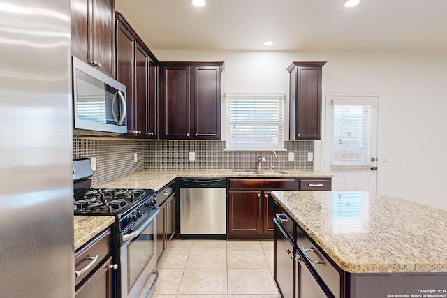 kitchen with decorative backsplash, appliances with stainless steel finishes, light stone counters, sink, and light tile patterned floors