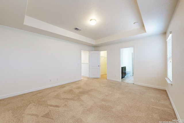 unfurnished bedroom with a raised ceiling, multiple windows, and light colored carpet