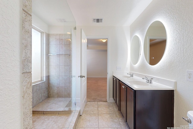 bathroom with tile patterned flooring, vanity, tiled shower, and plenty of natural light