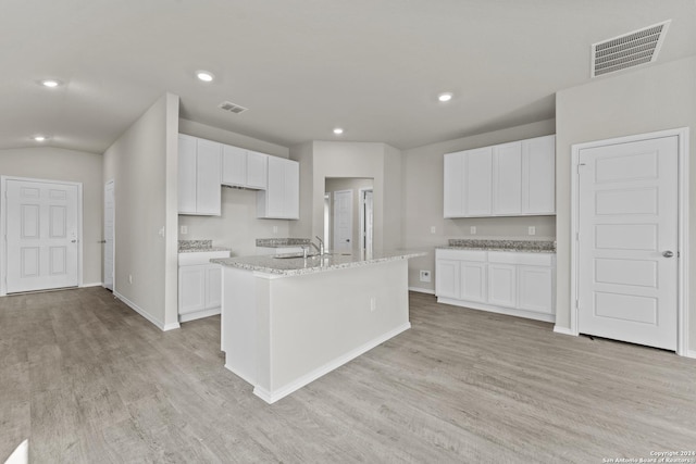 kitchen with white cabinets, light stone counters, an island with sink, and light wood-type flooring