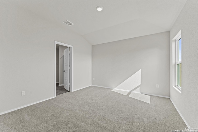 empty room featuring dark colored carpet, plenty of natural light, and lofted ceiling