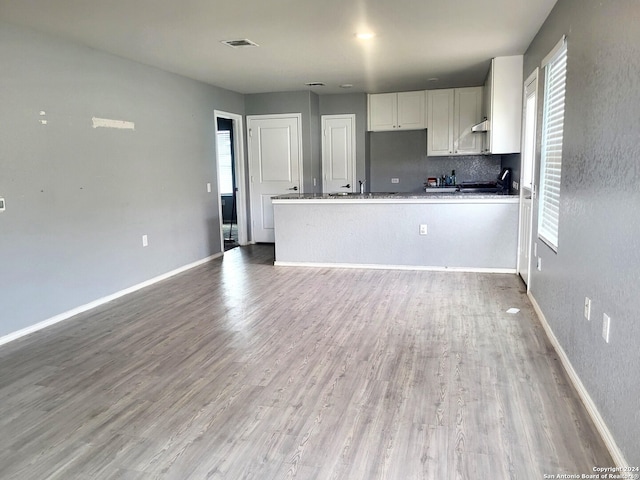 kitchen with tasteful backsplash, kitchen peninsula, white cabinets, and light wood-type flooring