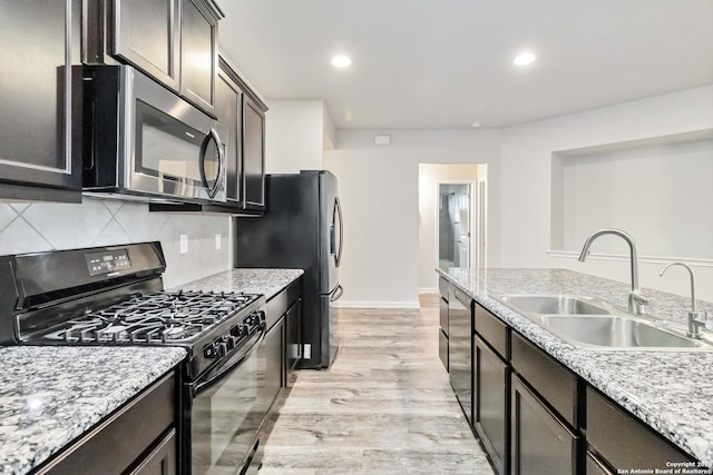 kitchen featuring black appliances, sink, light hardwood / wood-style flooring, decorative backsplash, and light stone countertops