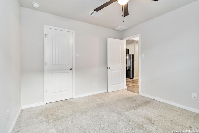 unfurnished bedroom with light colored carpet, stainless steel refrigerator, and ceiling fan