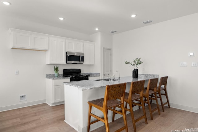 kitchen with a kitchen breakfast bar, kitchen peninsula, light hardwood / wood-style flooring, black gas range oven, and white cabinetry