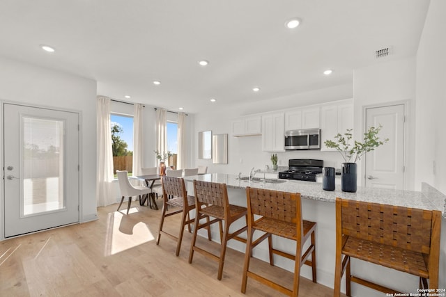 kitchen featuring light stone countertops, a kitchen breakfast bar, sink, white cabinets, and black gas range