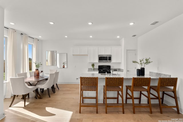 kitchen featuring a kitchen bar, light stone counters, black gas stove, light hardwood / wood-style floors, and white cabinetry