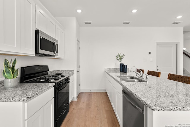 kitchen with light stone countertops, appliances with stainless steel finishes, sink, white cabinets, and light hardwood / wood-style floors