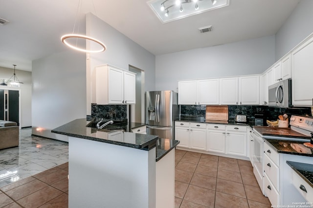 kitchen featuring kitchen peninsula, appliances with stainless steel finishes, backsplash, white cabinetry, and hanging light fixtures