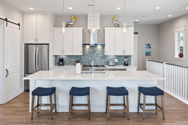 kitchen featuring white cabinets, decorative light fixtures, a barn door, and an island with sink