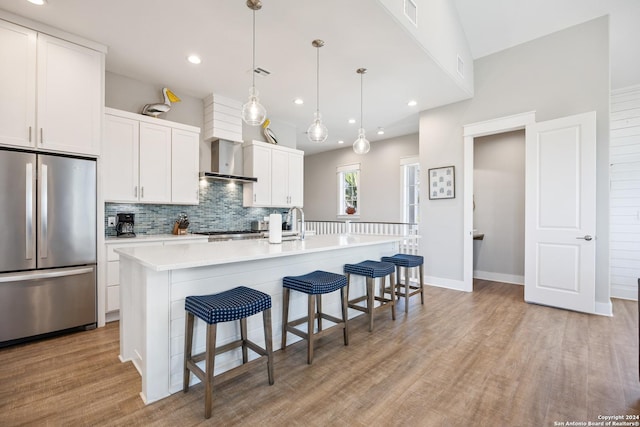 kitchen with a center island with sink, white cabinets, decorative backsplash, decorative light fixtures, and stainless steel refrigerator