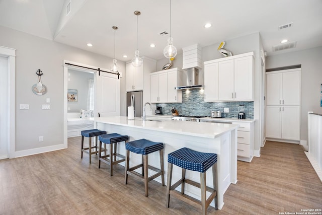 kitchen featuring white cabinetry, hanging light fixtures, stainless steel appliances, a barn door, and a kitchen island with sink