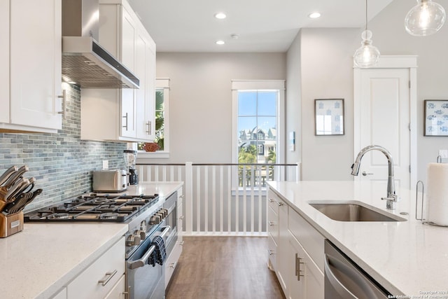 kitchen with white cabinets, sink, wall chimney exhaust hood, light stone counters, and stainless steel appliances