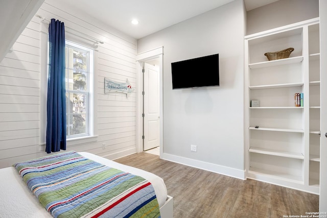 bedroom featuring multiple windows, wooden walls, and light wood-type flooring