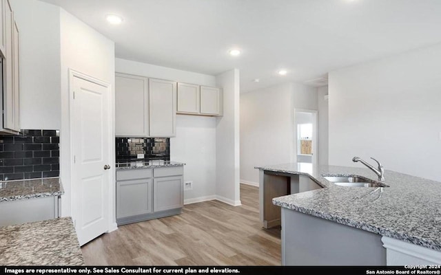 kitchen with backsplash, light hardwood / wood-style floors, light stone counters, and sink