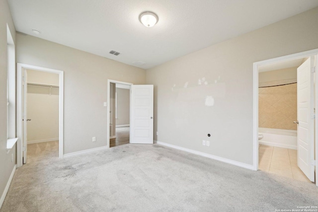 unfurnished bedroom with a walk in closet, connected bathroom, light colored carpet, and a closet