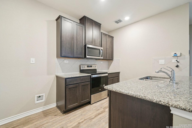 kitchen featuring sink, decorative backsplash, light stone countertops, appliances with stainless steel finishes, and dark brown cabinets