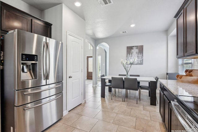 kitchen with stainless steel refrigerator with ice dispenser, stove, light stone counters, dark brown cabinets, and light tile patterned flooring