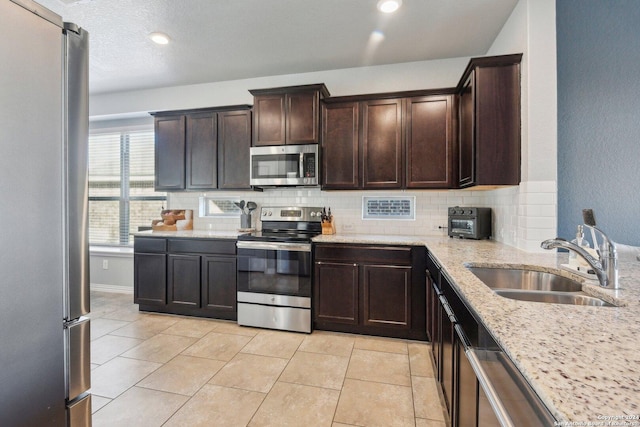 kitchen with appliances with stainless steel finishes, light stone counters, dark brown cabinets, sink, and light tile patterned floors