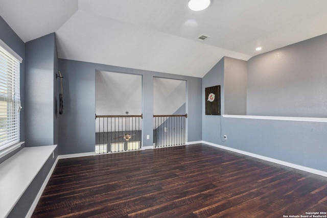 empty room featuring a healthy amount of sunlight, dark wood-type flooring, and vaulted ceiling