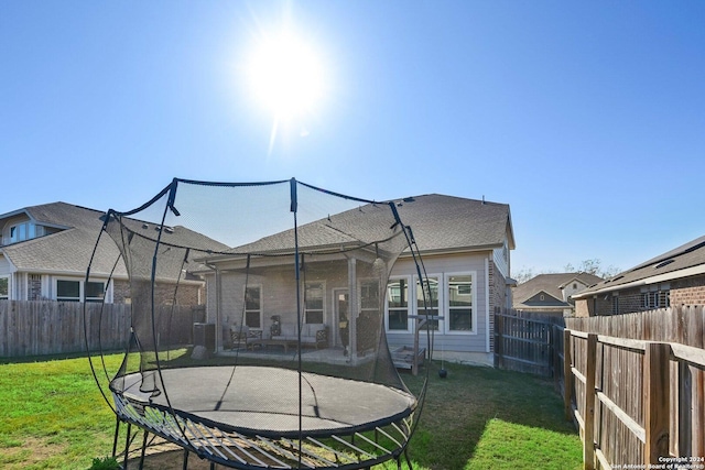 back of property with a trampoline and a lawn