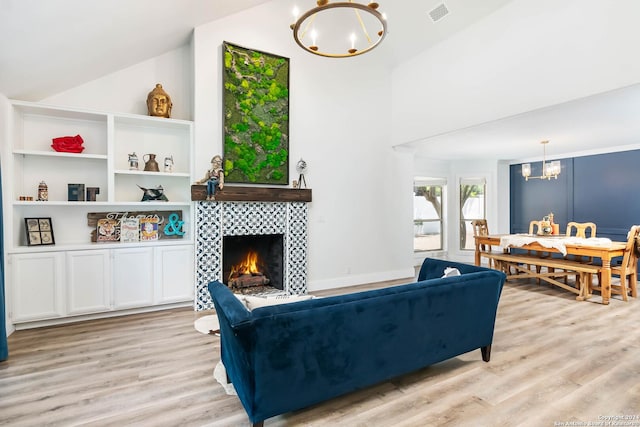 living room with vaulted ceiling, an inviting chandelier, light hardwood / wood-style floors, and a tiled fireplace