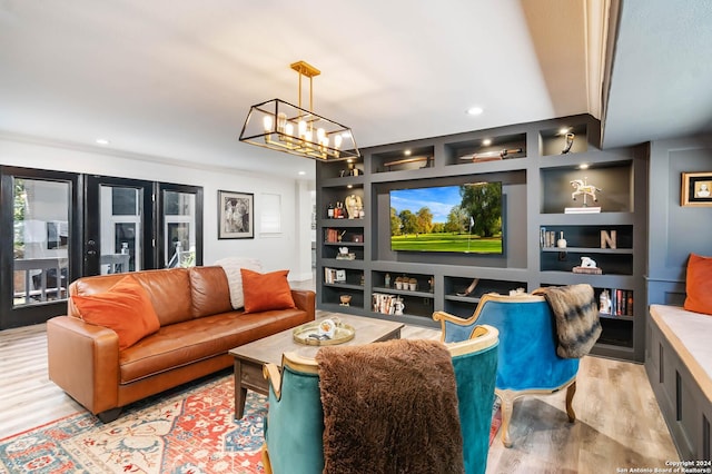 living room featuring built in shelves, light wood-type flooring, crown molding, and an inviting chandelier