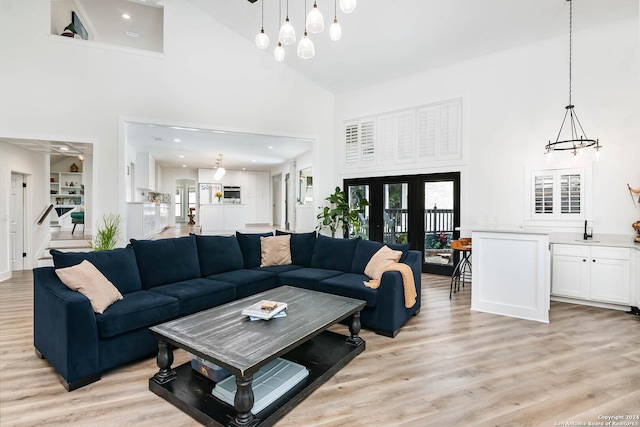 living room with sink, french doors, a high ceiling, an inviting chandelier, and light hardwood / wood-style floors