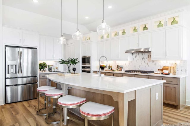 kitchen with backsplash, a center island with sink, hanging light fixtures, white cabinetry, and stainless steel appliances