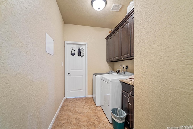 laundry area featuring washing machine and clothes dryer, light tile patterned floors, cabinets, and a textured ceiling