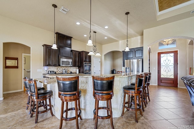 kitchen with light stone countertops, appliances with stainless steel finishes, dark brown cabinets, and a large island