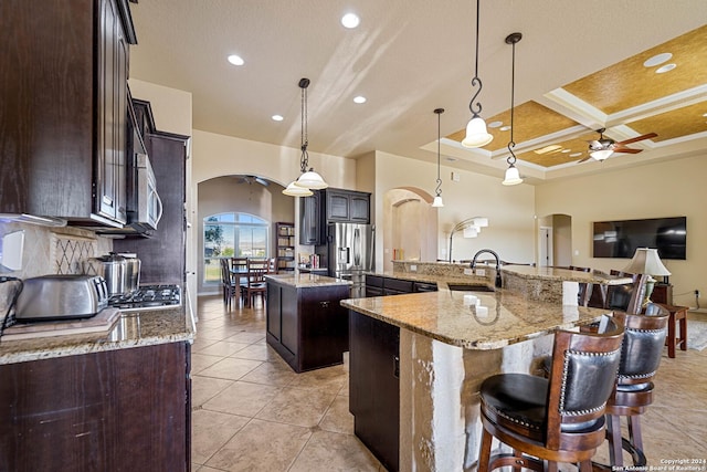 kitchen featuring appliances with stainless steel finishes, coffered ceiling, a large island with sink, decorative light fixtures, and beamed ceiling