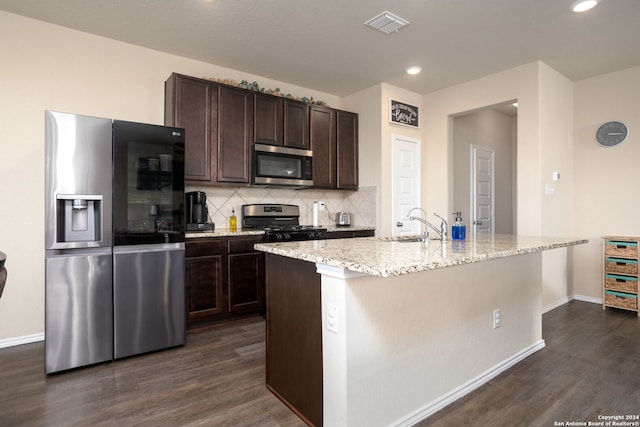 kitchen with a kitchen island with sink, dark brown cabinets, dark wood-type flooring, and appliances with stainless steel finishes